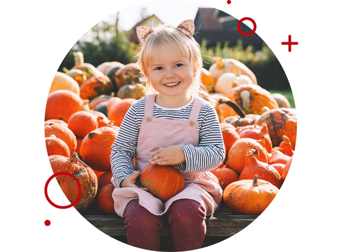 A little girl sitting in a pumpkin patch smiling.