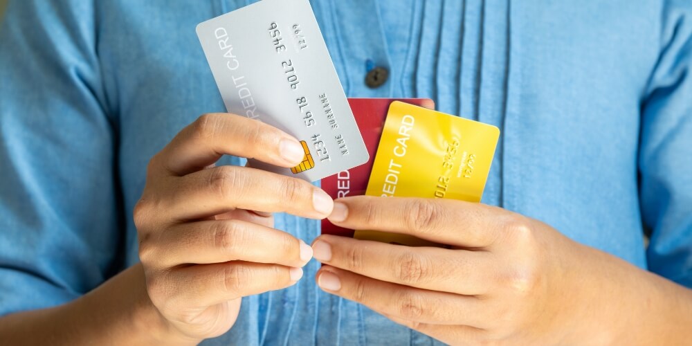 Close-up of a person in a blue shirt holding multiple credit cards in their hands.