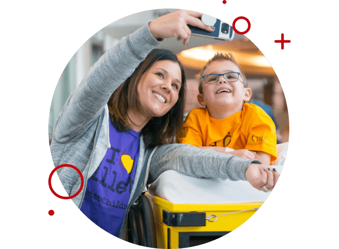 Smiling woman taking a selfie with a boy in a wheelchair wearing glasses and a bright yellow t-shirt.